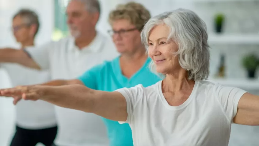 older humans in a yoga pose with their arms stretching forward and back