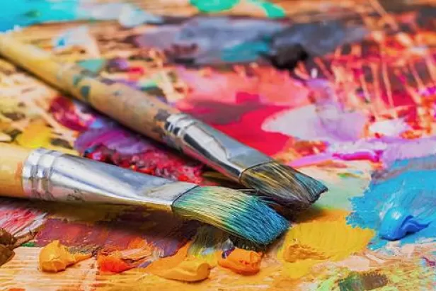ikmage of paint brushes covered in paint on a board with paint smeared in all different colors