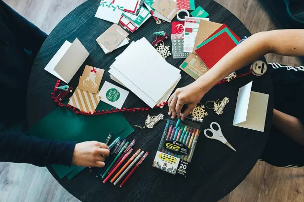 over head picture of people creating paper greeting cards on a green tablecloth
