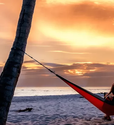 A person on a hammock between two palm trees during sunset at Sanibel Island