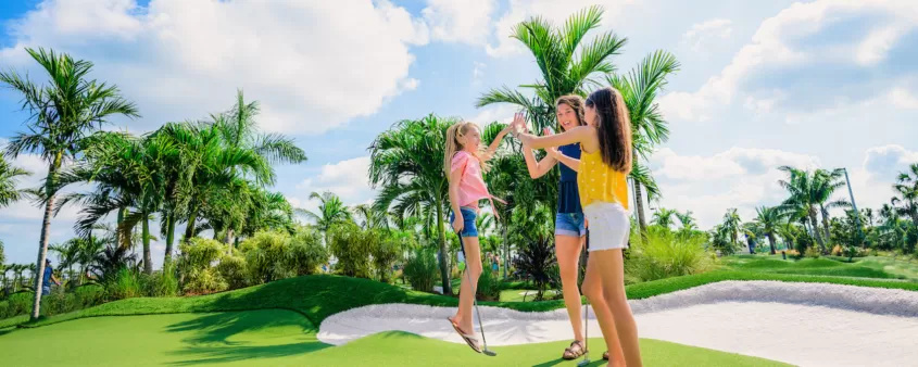 A mom and two daughters high-five at the hole at popstroke putting course