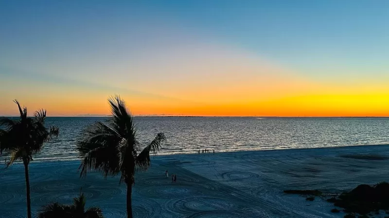 sunset on Fort Myers Beach with two palm trees sillhoutes in view