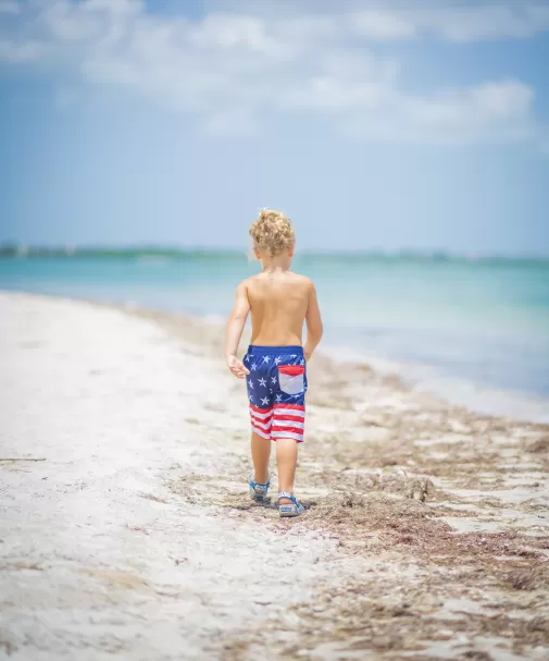 A boy at a beach with American flag swim trunks